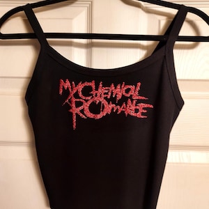 Puede incluir: Camiseta sin mangas negra con tirantes finos y el texto "MY CHEMICAL ROMANCE" en letras rojas brillantes. La camiseta está colgada en una percha negra contra una puerta blanca.