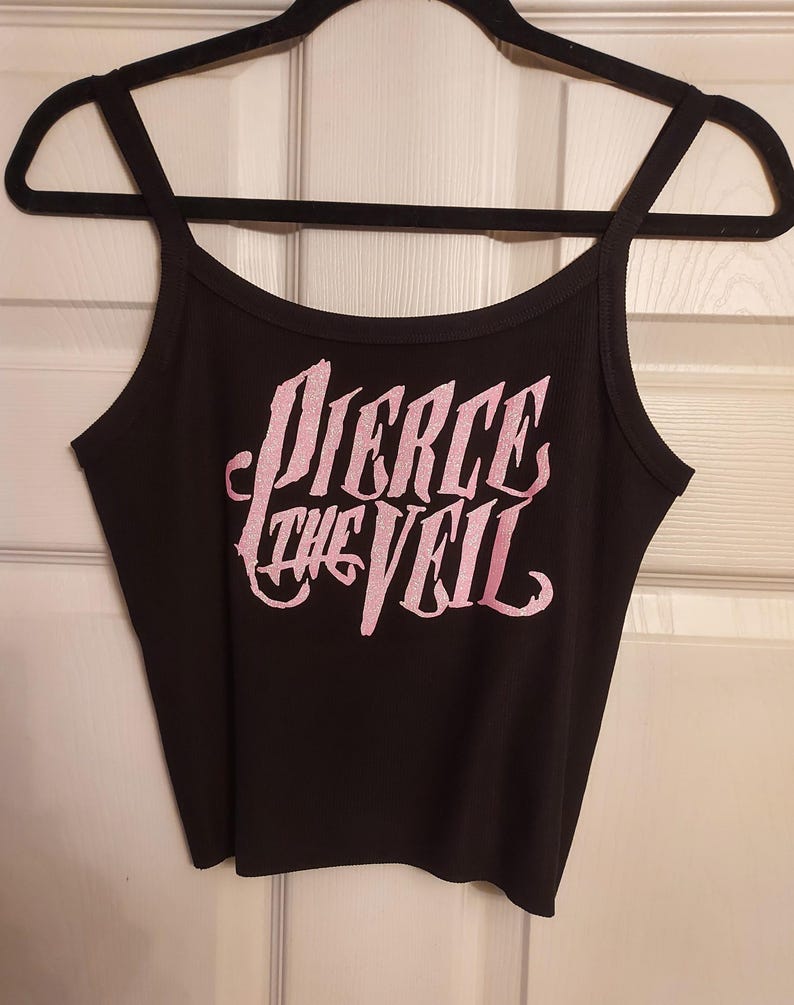 Puede incluir: Top negro de tirantes con un dise&ntilde;o de purpurina rosa que dice "Pierce the Veil".