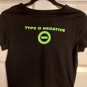 Puede incluir: Camiseta negra recortada con un gr&aacute;fico verde del logotipo de la banda Type O Negative, un c&iacute;rculo con una l&iacute;nea horizontal.