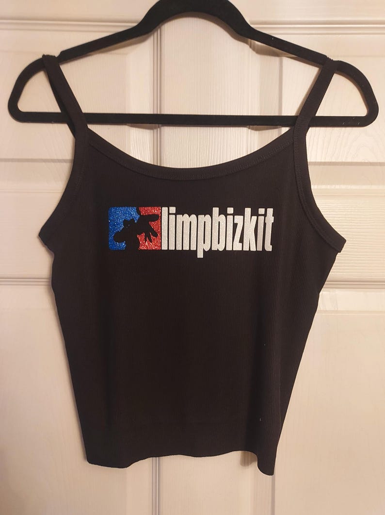 Puede incluir: Top negro de tirantes finos con un logotipo "limp bizkit" de purpurina plateada y un gr&aacute;fico rojo, blanco y azul.