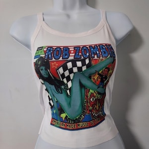 Puede incluir: Camiseta blanca de tirantes con un estampado gr&aacute;fico colorido de una mujer y el texto "Rob Zombie American Made Music to Strike By".
