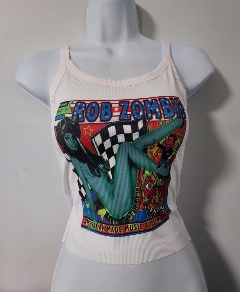 Puede incluir: Camiseta blanca de tirantes con un estampado gr&aacute;fico colorido de una mujer y el texto "Rob Zombie American Made Music to Strike By".