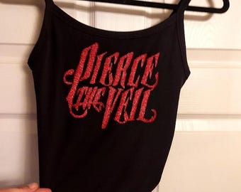 Puede incluir: Camiseta sin mangas negra con tirantes finos y el texto "Pierce the Veil" en letras rojas brillantes. La camiseta está colgada de una percha negra contra una puerta blanca.