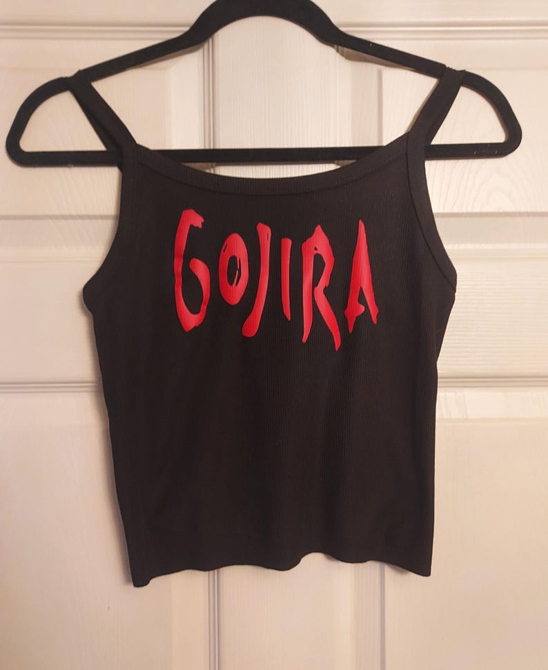 Puede incluir: Top negro de tirantes finos con la palabra "GOJIRA" impresa en rojo en la parte delantera.