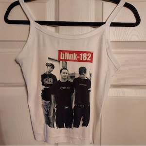 Op de afbeelding: Wit tanktop met een zwart-witte afbeelding van de band blink-182. De bandleden dragen zwarte shirts en jeans. De naam van de band is in rode letters op een witte achtergrond gedrukt.