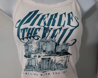 May include: Cream-colored ribbed tank top with thin straps. The front features the teal text "PIERCE THE VEIL" above a detailed illustration of a dilapidated house. Below the house, the text reads "COLLIDE WITH THE SKY."