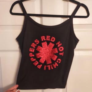 Puede incluir: Camiseta negra de tirantes con un logotipo de "Red Hot Chili Peppers" en lentejuelas rojas.