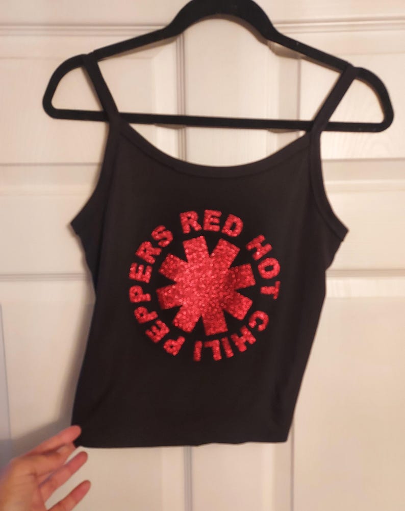 Puede incluir: Camiseta negra de tirantes con un logotipo de "Red Hot Chili Peppers" en lentejuelas rojas.