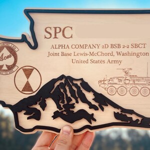 May include: Wooden plaque in the shape of Washington State, with black trim. The plaque features the text "SPC", "ALPHA COMPANY 2D BSB 2-2 SBCT", and "Joint Base Lewis-McChord, Washington, United States Army". Includes a mountain silhouette and military vehicle.