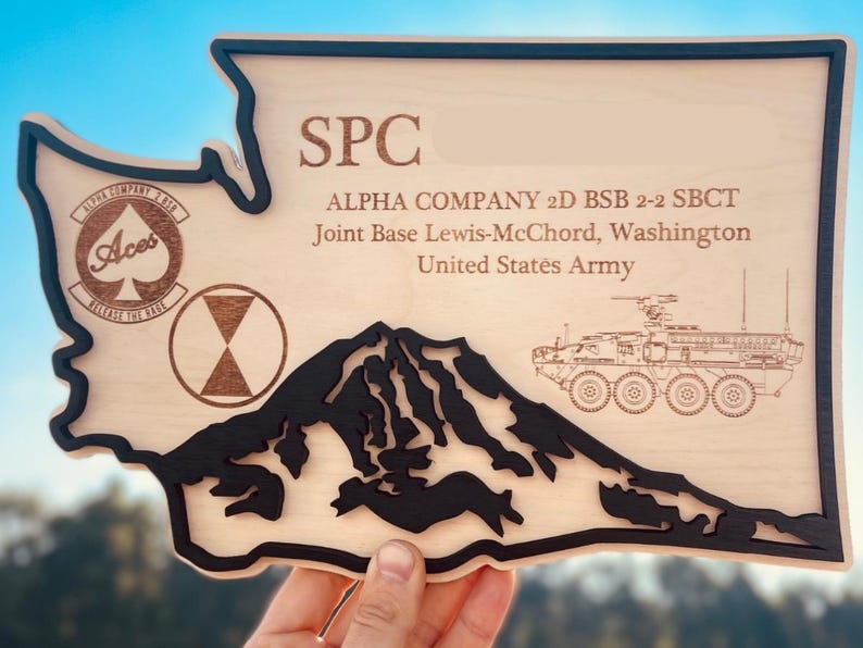 May include: Wooden plaque in the shape of Washington State, with black trim. The plaque features the text "SPC", "ALPHA COMPANY 2D BSB 2-2 SBCT", and "Joint Base Lewis-McChord, Washington, United States Army". Includes a mountain silhouette and military vehicle.