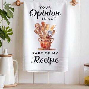 Pode incluir: Toalha de cozinha branca com o texto "Your Opinion Is Not Part Of My Recipe" em letras pretas. Uma ilustra&ccedil;&atilde;o em aquarela de utens&iacute;lios de cozinha de madeira em uma panela marrom est&aacute; no centro da toalha.