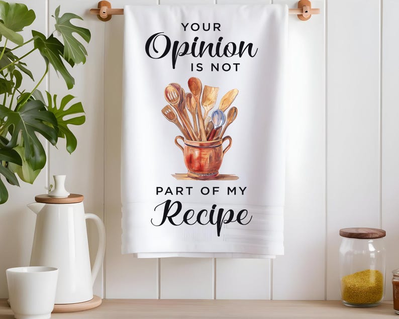 Pode incluir: Toalha de cozinha branca com o texto "Your Opinion Is Not Part Of My Recipe" em letras pretas. Uma ilustra&ccedil;&atilde;o em aquarela de utens&iacute;lios de cozinha de madeira em uma panela marrom est&aacute; no centro da toalha.