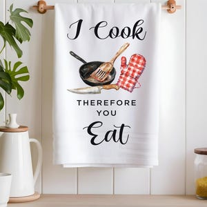 Pode incluir: Toalha de cozinha branca com o texto "I Cook Therefore You Eat" em preto. A toalha apresenta uma ilustra&ccedil;&atilde;o em aquarela de uma panela, uma esp&aacute;tula e uma luva de forno.
