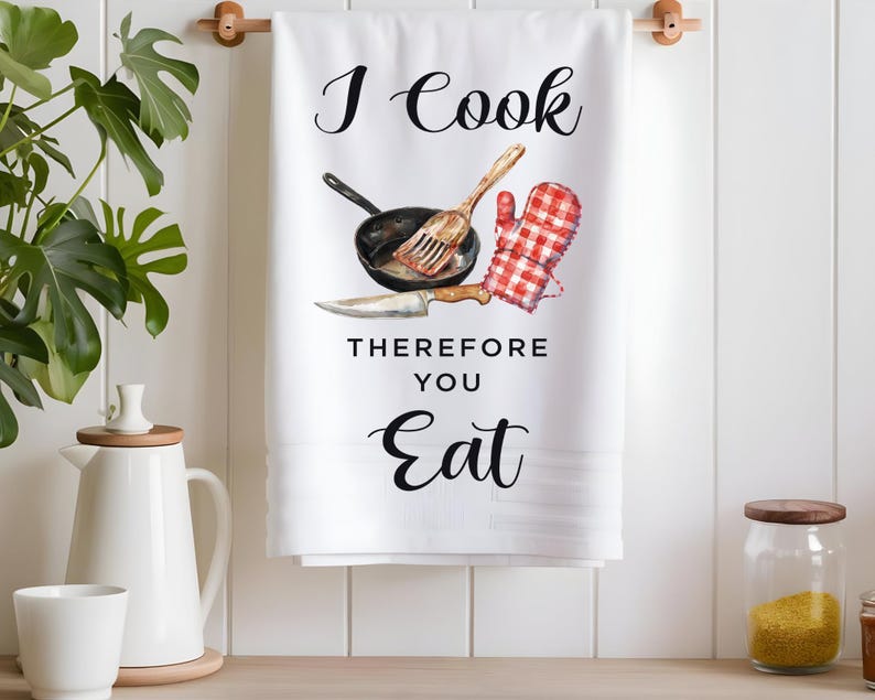 Pode incluir: Toalha de cozinha branca com o texto "I Cook Therefore You Eat" em preto. A toalha apresenta uma ilustra&ccedil;&atilde;o em aquarela de uma panela, uma esp&aacute;tula e uma luva de forno.