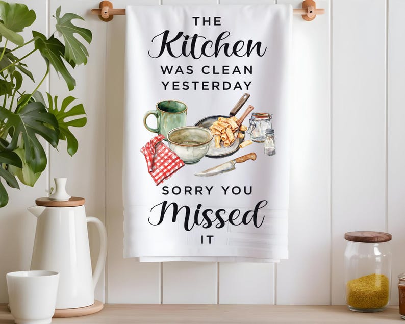 Pode incluir: Toalha de cozinha branca com texto preto que diz "The Kitchen Was Clean Yesterday Sorry You Missed It". A toalha apresenta uma ilustra&ccedil;&atilde;o em aquarela de utens&iacute;lios de cozinha, uma tigela de macarr&atilde;o e uma caneca.
