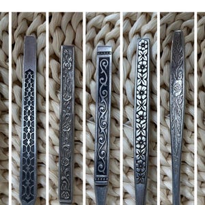 May include: Close-up of several antique silver flatware pieces. Each piece features a unique decorative pattern, including floral, geometric, and scroll designs. The silverware is arranged against a textured, woven background.