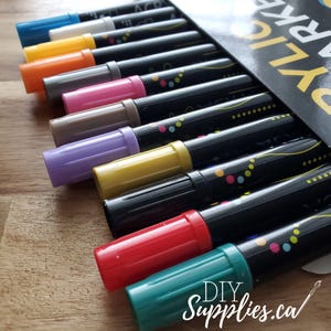 May include: A set of 12 black permanent markers with colourful caps. The caps are arranged in a rainbow pattern. The markers are labelled "DIY Supplies.ca".