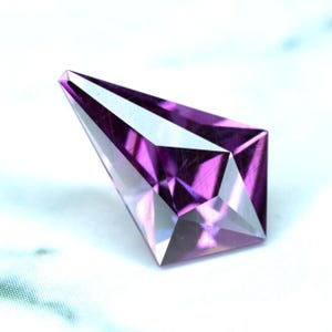 May include: A faceted purple amethyst gemstone with a pointed tip and a rectangular base.