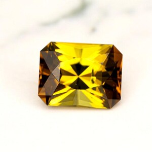 May include: A yellow and brown gemstone with a rectangular cut and a faceted design.