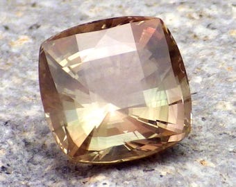 May include: A light brown, faceted gemstone with a square shape. The gemstone has a slight green hue and is cut to reflect light.