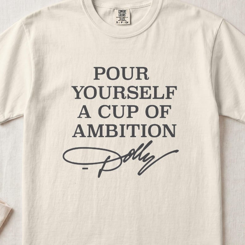 Cream t-shirt with "POUR YOURSELF A CUP OF AMBITION Dolly" text.