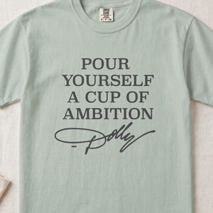 Light green t-shirt with "Pour Yourself a Cup of Ambition Dolly" printed.
