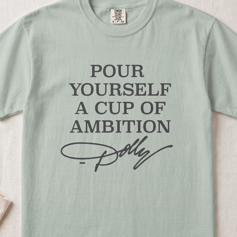 Light green t-shirt with "Pour Yourself a Cup of Ambition Dolly" printed.