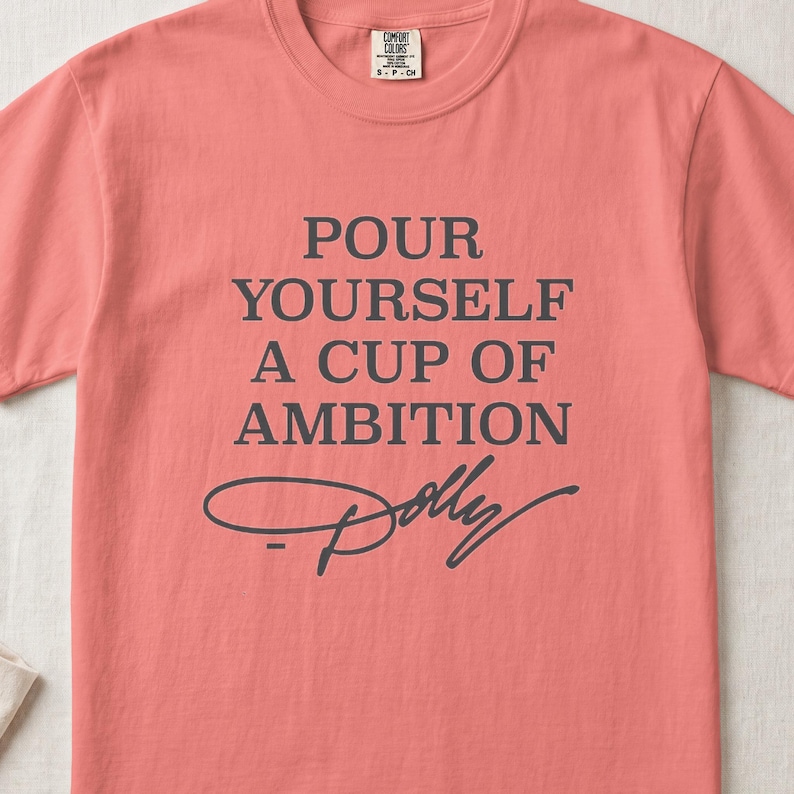 Coral t-shirt with "Pour Yourself A Cup Of Ambition Dolly" text.