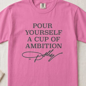 Pink t-shirt with gray text "Pour Yourself A Cup Of Ambition Dolly"