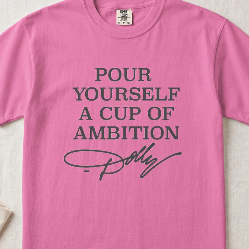 Pink t-shirt with gray text "Pour Yourself A Cup Of Ambition Dolly"