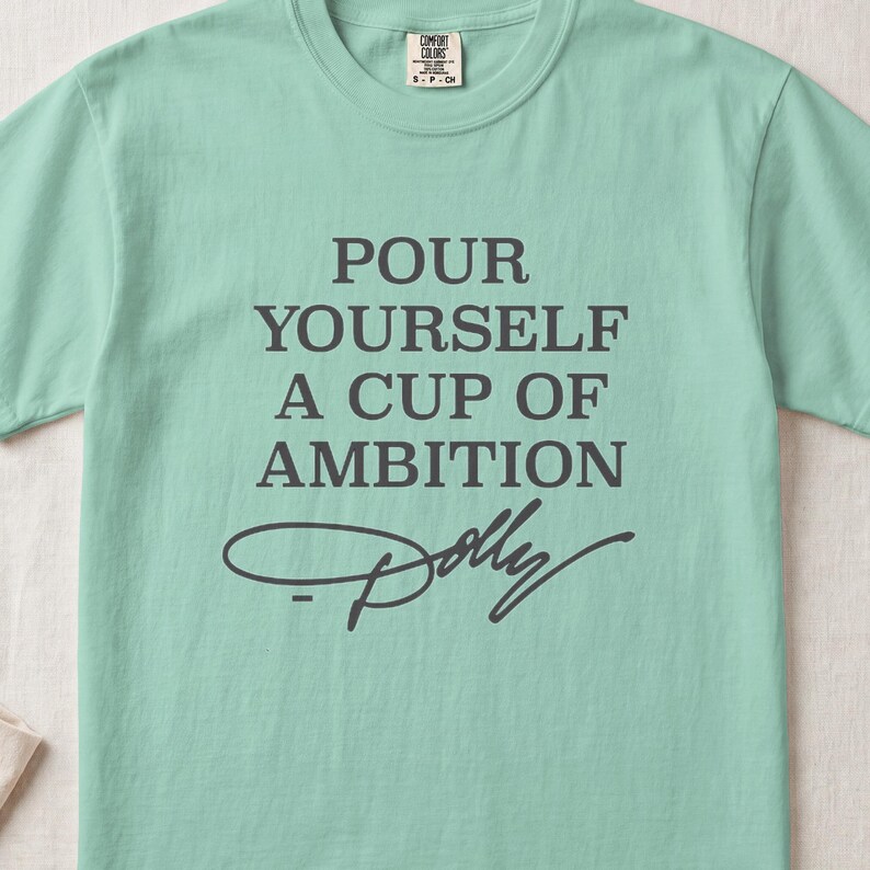 Mint green t-shirt with "POUR YOURSELF A CUP OF AMBITION Dolly" text.