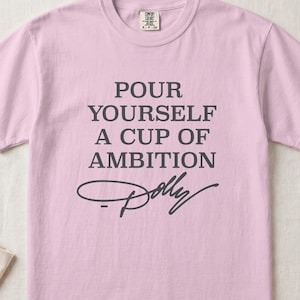 Pink Comfort Colors t-shirt with text "Pour Yourself a Cup of Ambition" and Dolly's signature.