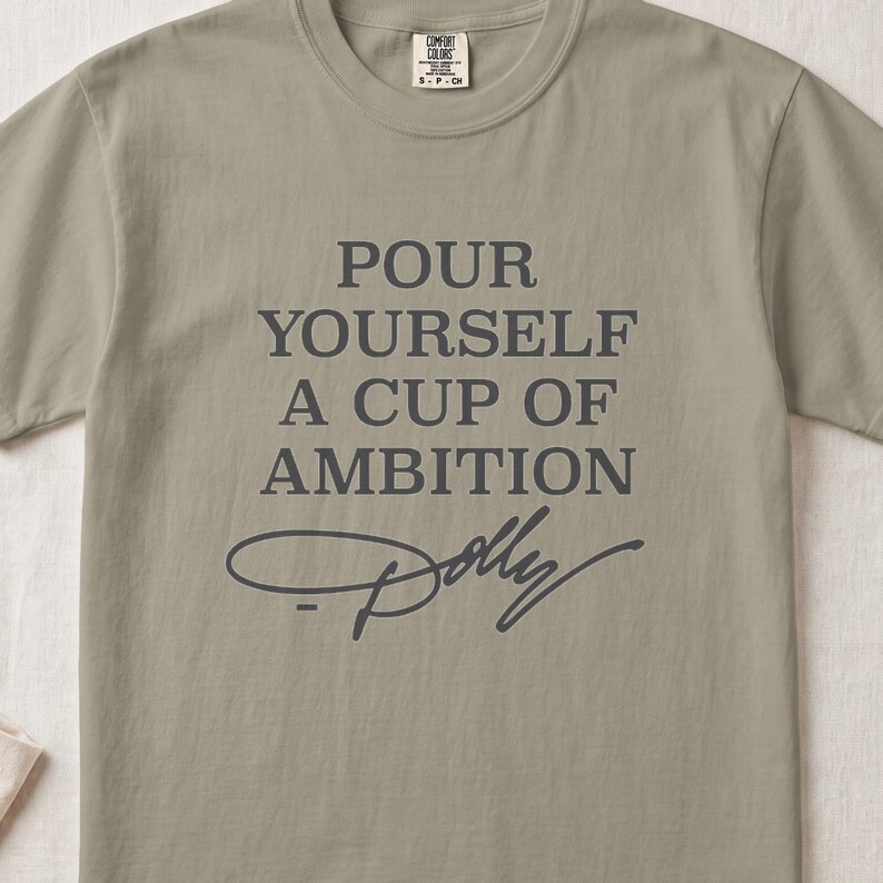 T-shirt with text "POUR YOURSELF A CUP OF AMBITION" and Dolly Parton's signature.