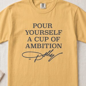 Mustard t-shirt with "Pour Yourself A Cup Of Ambition Dolly" text.