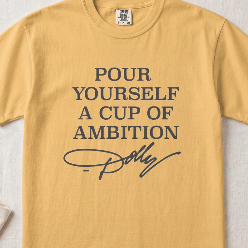 Mustard t-shirt with "Pour Yourself A Cup Of Ambition Dolly" text.