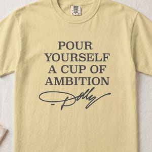 Light yellow t-shirt with "POUR YOURSELF A CUP OF AMBITION Dolly" text.