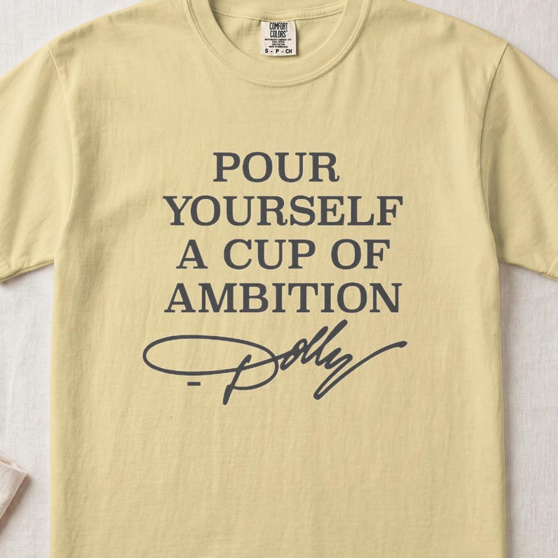 Light yellow t-shirt with "POUR YOURSELF A CUP OF AMBITION Dolly" text.
