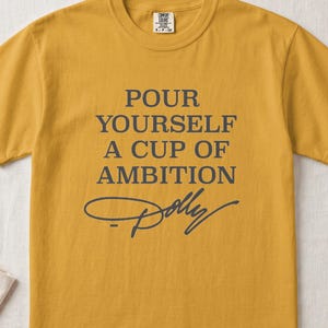 Mustard yellow t-shirt with "Pour Yourself A Cup of Ambition Dolly" text.