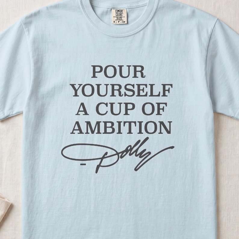 Light blue t-shirt with "Pour Yourself A Cup Of Ambition" and "Dolly" signature.