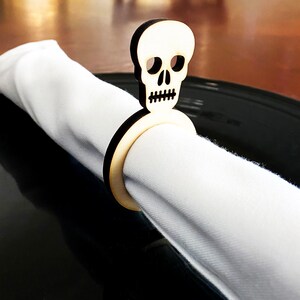May include: A wooden napkin ring shaped like a skull with a black ring. The ring is holding a white napkin.