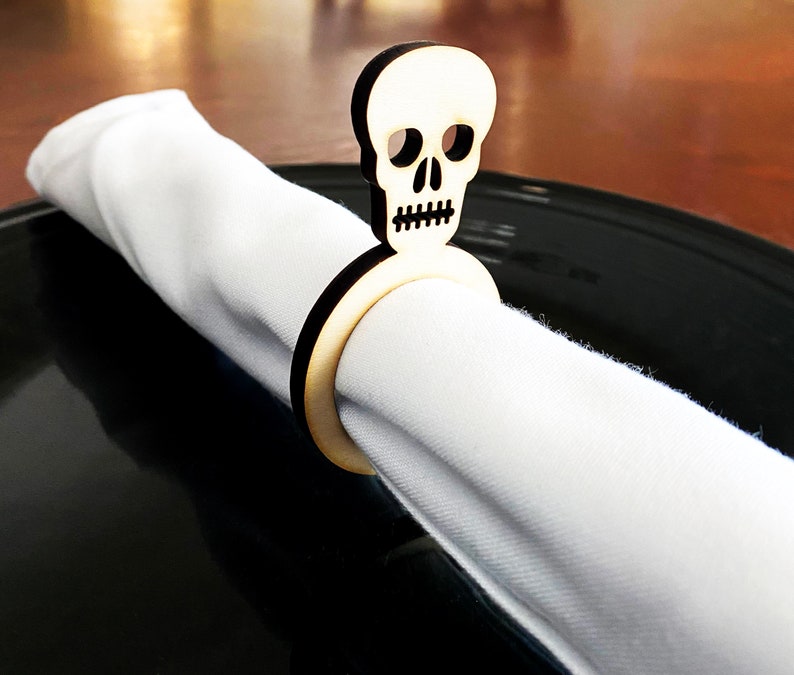 May include: A wooden napkin ring shaped like a skull with a black ring. The ring is holding a white napkin.