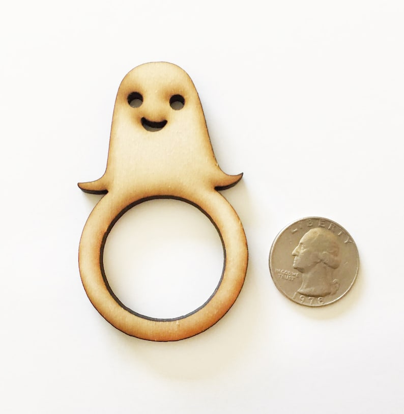 May include: Wooden ghost napkin ring with a smiling face. The ring is about the size of a US quarter.