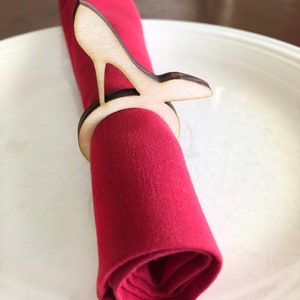 May include: A wooden napkin ring shaped like a high heel shoe. The ring is holding a red napkin.