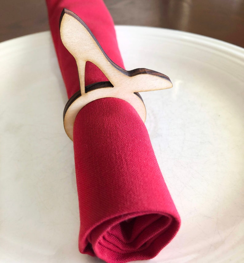 May include: A wooden napkin ring shaped like a high heel shoe. The ring is holding a red napkin.