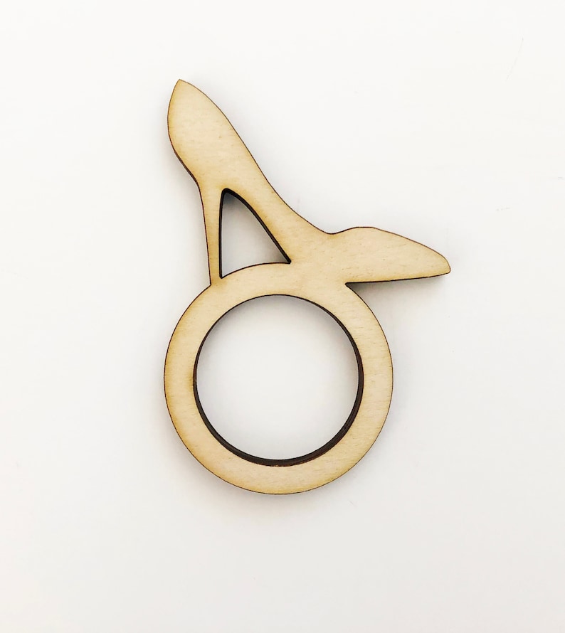 May include: A wooden napkin ring shaped like a high-heeled shoe. The ring is light brown and has a smooth finish.