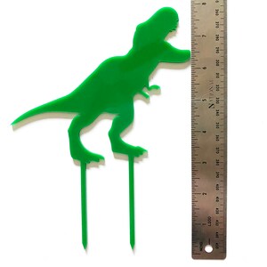 May include: Green plastic dinosaur cake topper with two skewers. The dinosaur is approximately 6 inches tall.