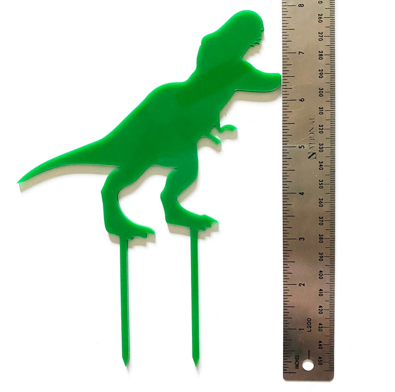 May include: Green plastic dinosaur cake topper with two skewers. The dinosaur is approximately 6 inches tall.