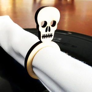 May include: A wooden napkin ring shaped like a skull with a white napkin. The skull is carved with eye sockets, a nose, and a mouth.