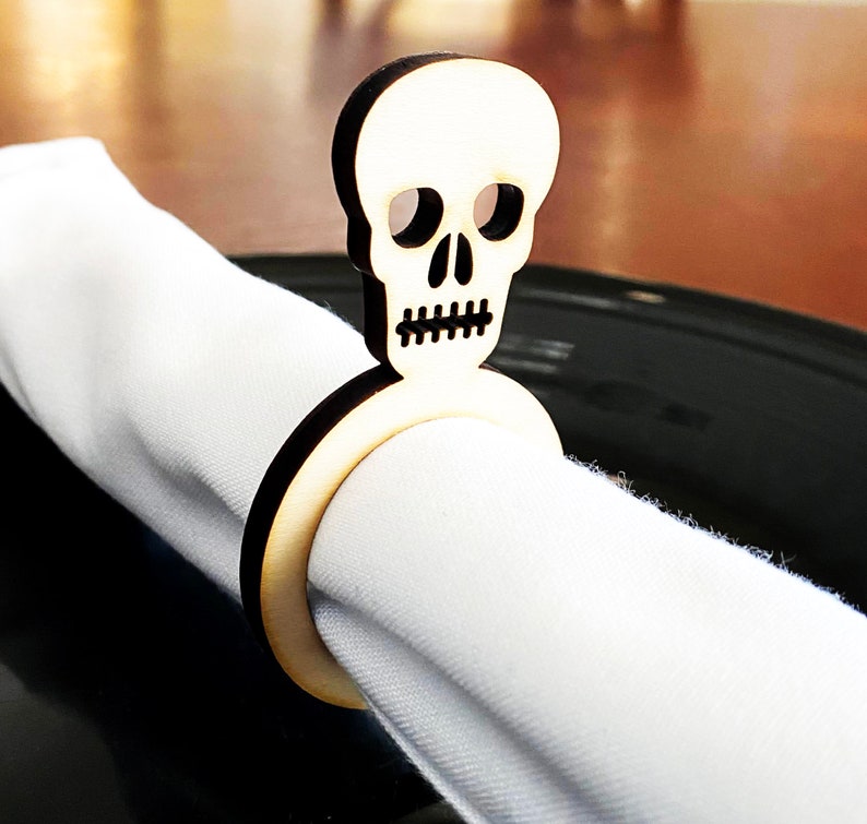 May include: A wooden napkin ring shaped like a skull with a white napkin. The skull is carved with eye sockets, a nose, and a mouth.