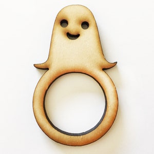 May include: A wooden ghost napkin ring with a smiling face. The ring is light brown and has a smooth finish.